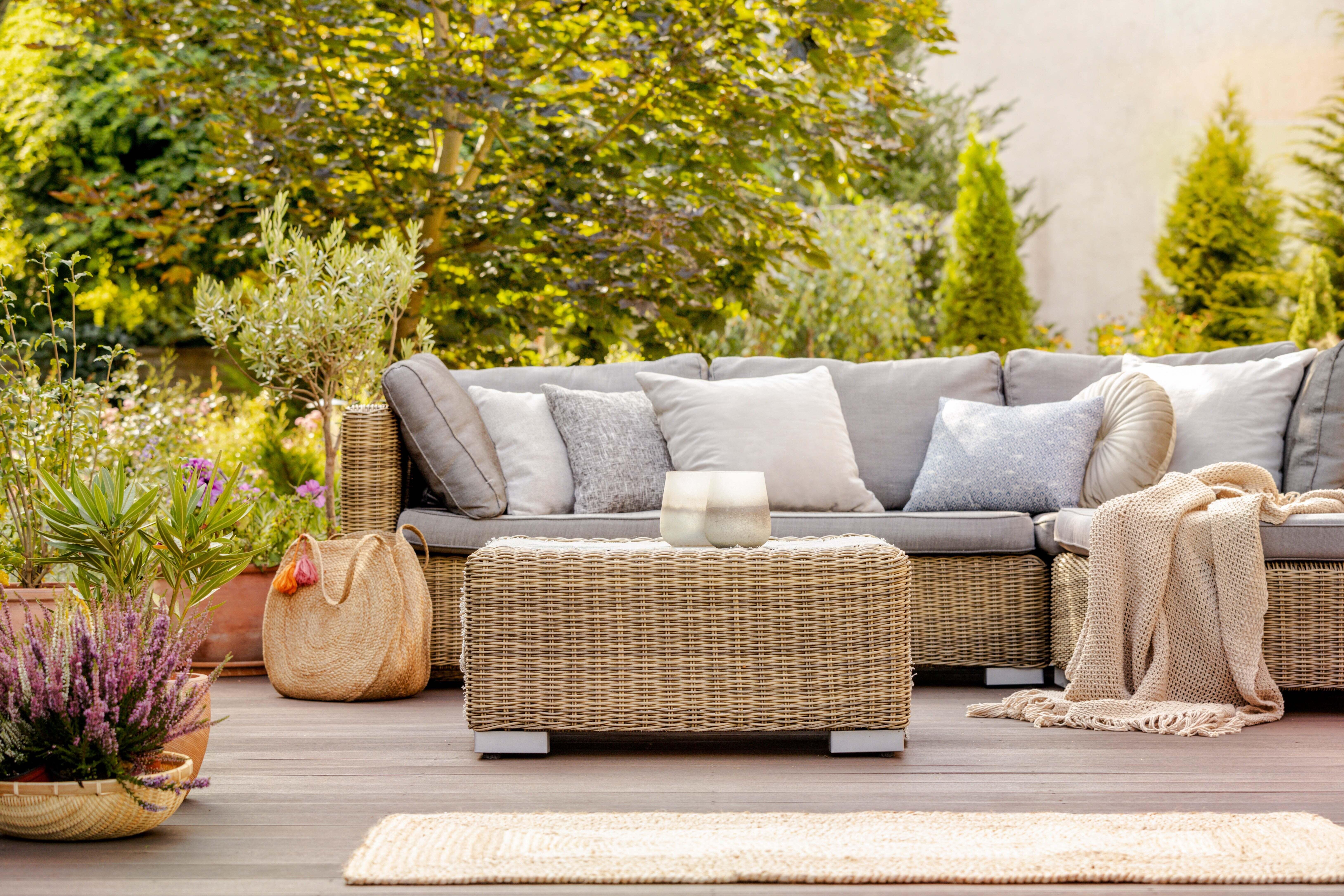 An outdoor patio furniture set is surrounded by plants and trees.