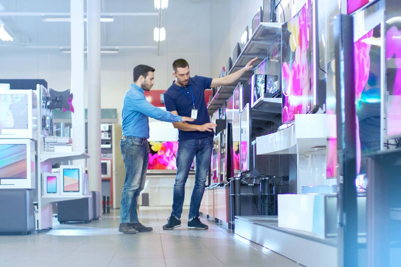 A man is shopping for TVs in a store and is talking to a salesperson.
