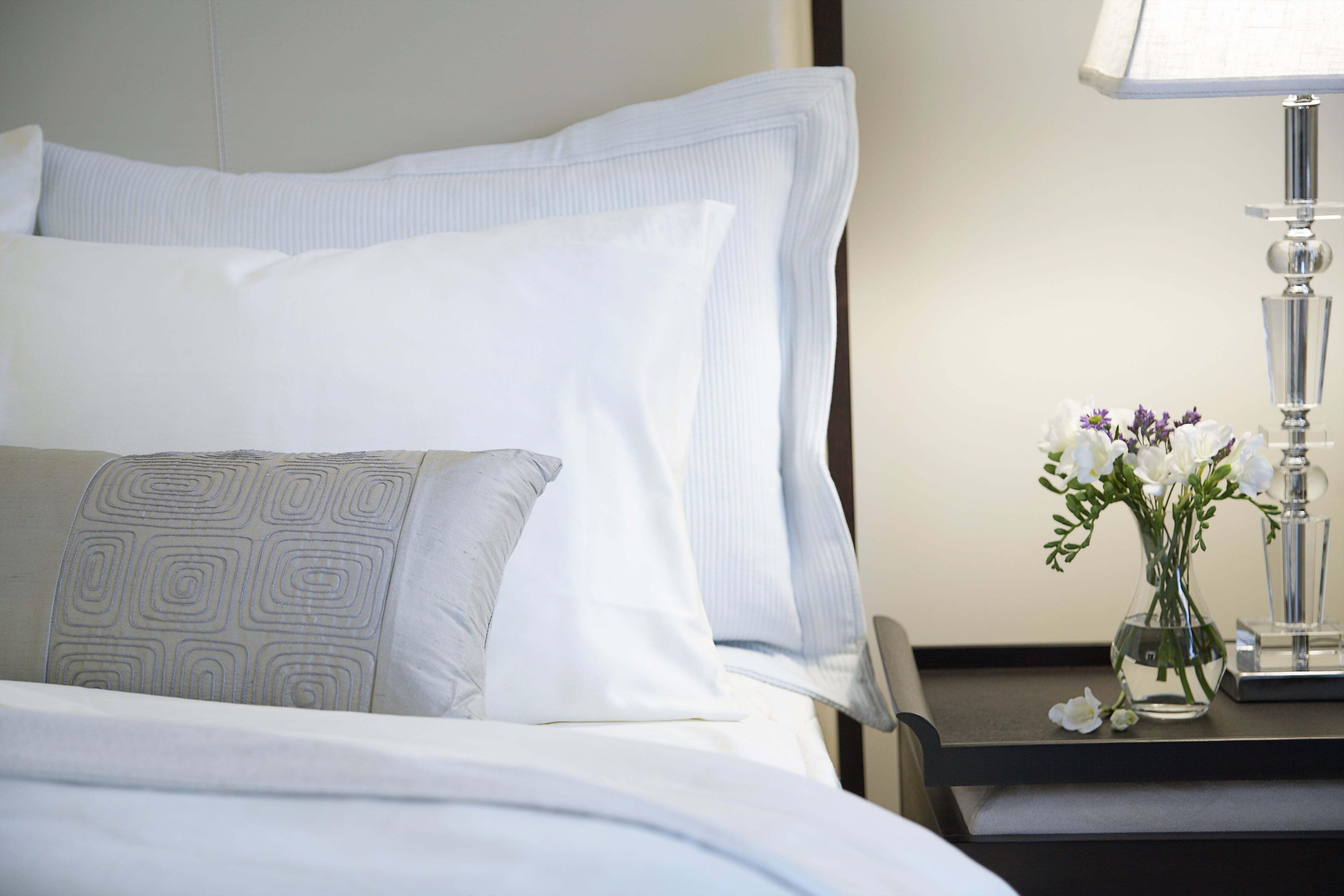 A well-made bed next to a nightstand with flowers on it