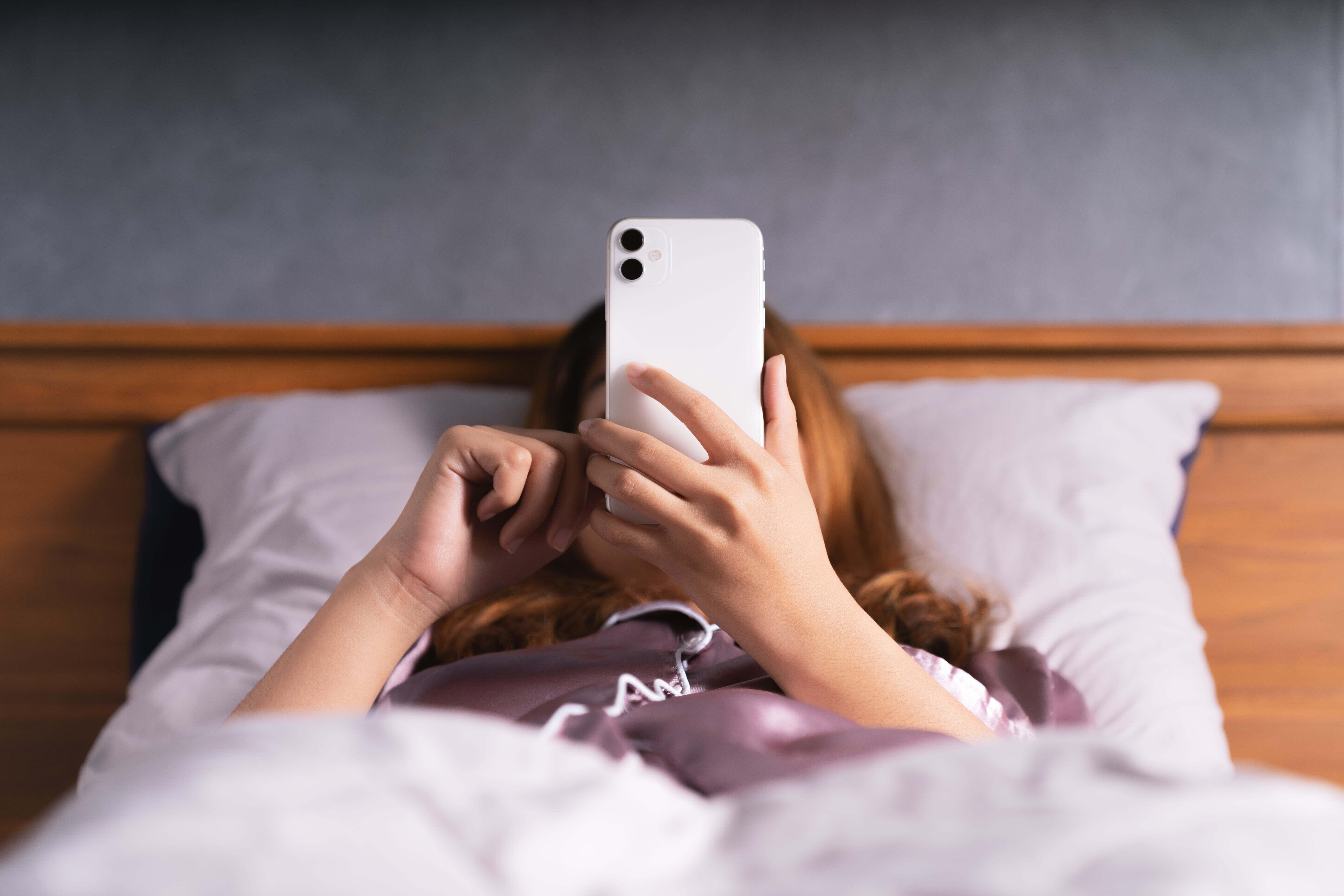 A woman laying in bed looking at her phone.
